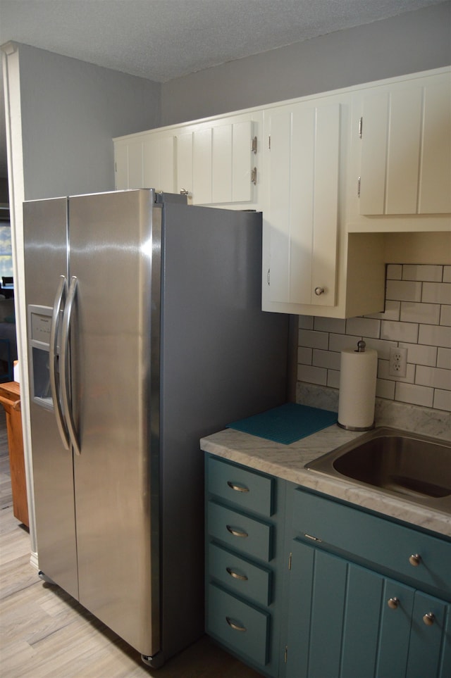 kitchen featuring light wood-type flooring, a textured ceiling, stainless steel fridge with ice dispenser, tasteful backsplash, and white cabinetry