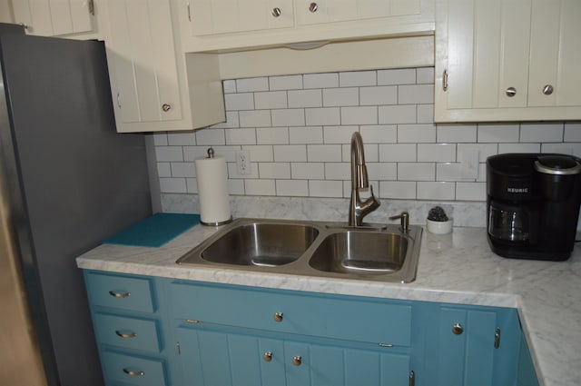 kitchen with blue cabinets, stainless steel fridge, sink, backsplash, and light stone countertops