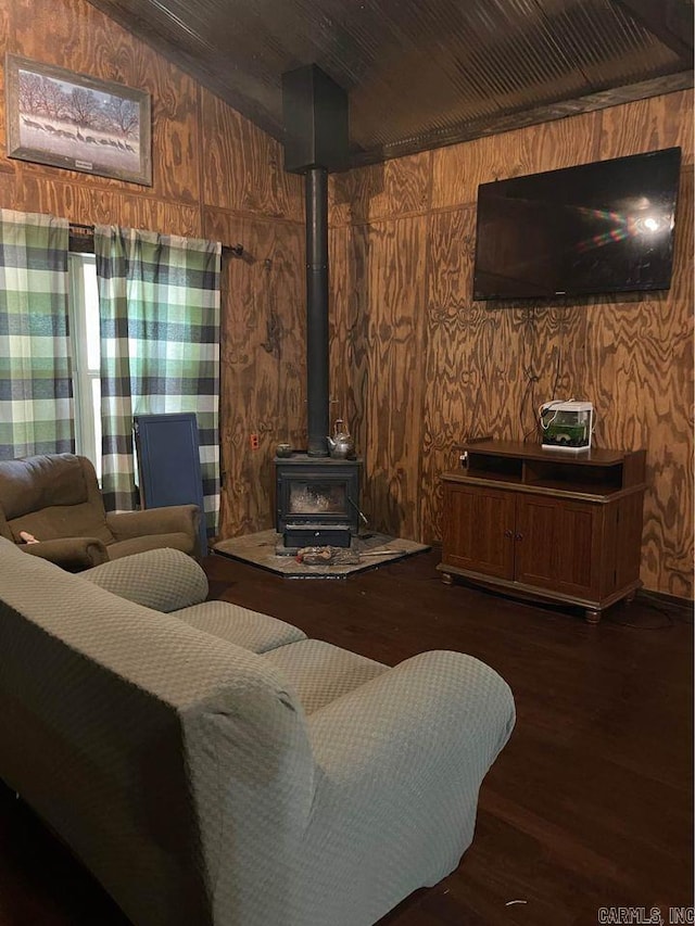 living room featuring lofted ceiling, a wood stove, dark wood-type flooring, and wooden walls