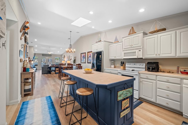 kitchen with white cabinets, hanging light fixtures, white appliances, a kitchen island, and light hardwood / wood-style floors