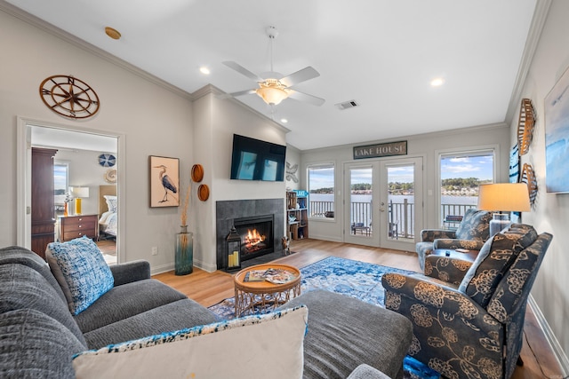 living room with a fireplace, light hardwood / wood-style flooring, ornamental molding, ceiling fan, and french doors