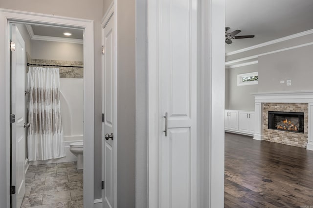 bathroom with shower / bathtub combination with curtain, a stone fireplace, crown molding, hardwood / wood-style floors, and toilet