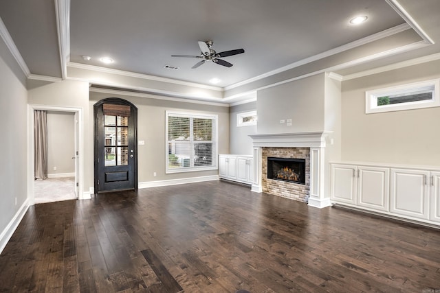 unfurnished living room with ceiling fan, a stone fireplace, crown molding, and dark hardwood / wood-style floors