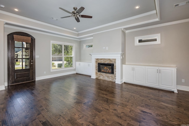 unfurnished living room featuring a tray ceiling, a fireplace, dark hardwood / wood-style flooring, ornamental molding, and ceiling fan