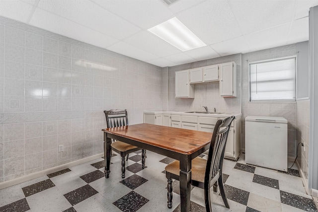 dining room with a paneled ceiling, tile walls, and sink