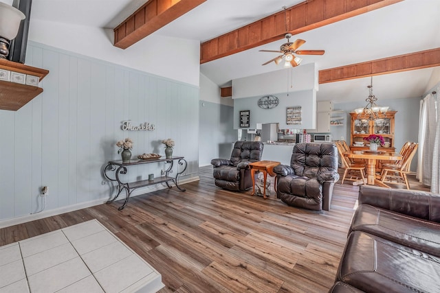 living room with high vaulted ceiling, ceiling fan with notable chandelier, light wood-type flooring, beam ceiling, and wooden walls