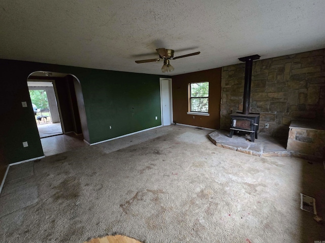 unfurnished living room featuring ceiling fan, a textured ceiling, a wood stove, and carpet