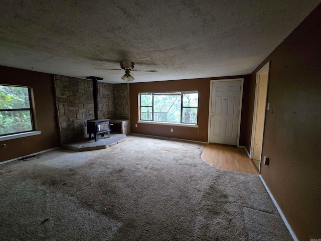 unfurnished living room featuring a textured ceiling, carpet flooring, ceiling fan, and a wood stove