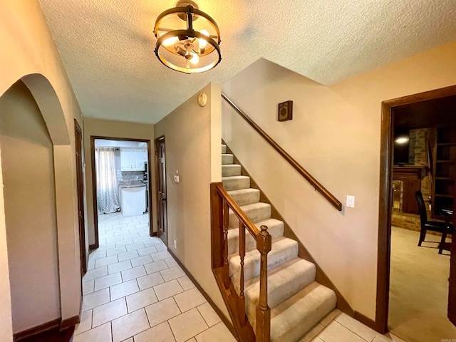 staircase featuring a notable chandelier, a textured ceiling, and tile patterned floors