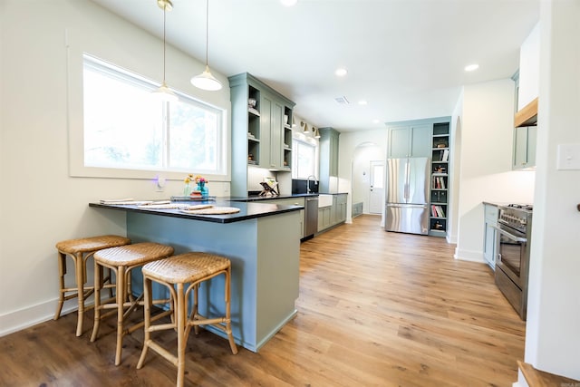 kitchen featuring light wood-type flooring, kitchen peninsula, appliances with stainless steel finishes, and decorative light fixtures