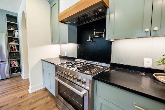 kitchen featuring light wood-type flooring, green cabinetry, appliances with stainless steel finishes, and custom range hood