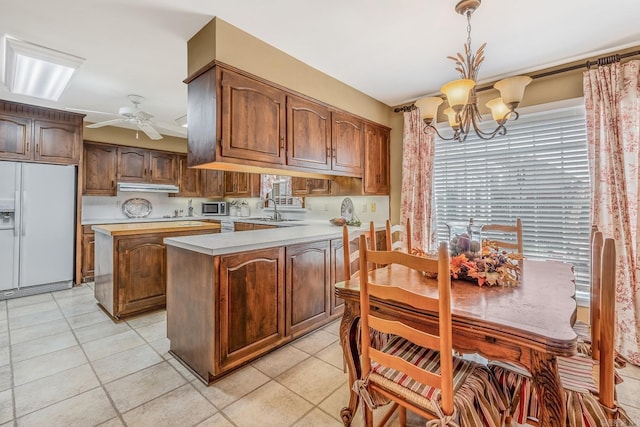 kitchen with white fridge with ice dispenser, sink, ceiling fan with notable chandelier, a kitchen island, and decorative light fixtures