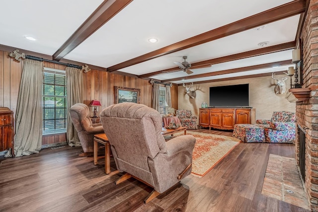 living room featuring dark wood-type flooring, beam ceiling, a brick fireplace, wooden walls, and ceiling fan