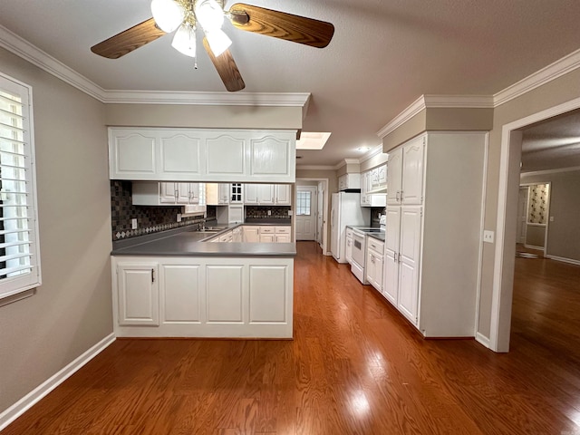 kitchen featuring a wealth of natural light, kitchen peninsula, white appliances, and white cabinetry