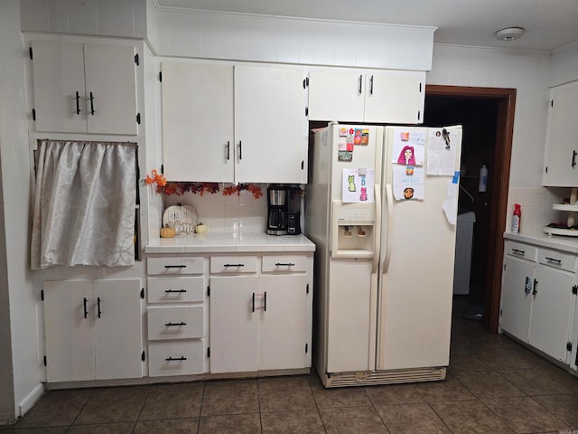 kitchen featuring white fridge with ice dispenser, white cabinets, dark tile patterned flooring, and tasteful backsplash