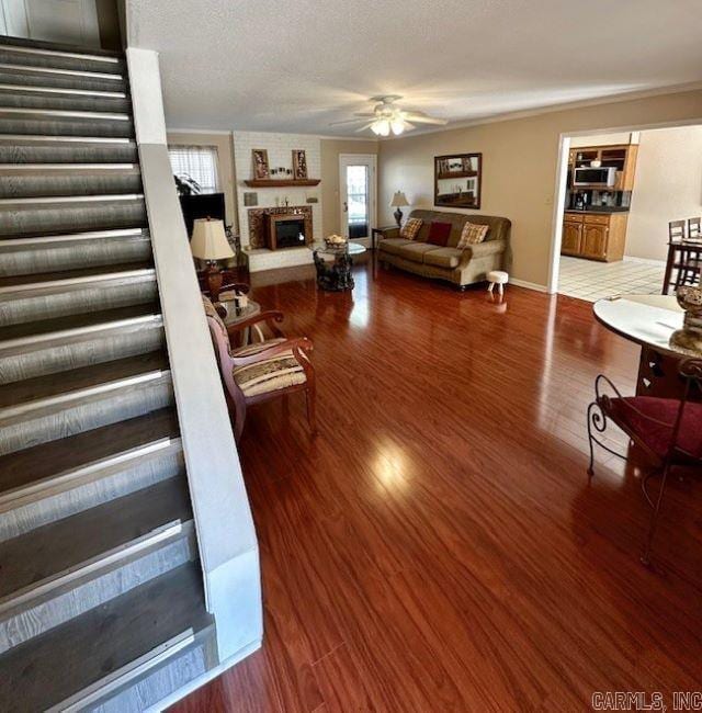 living room with ceiling fan, wood-type flooring, a textured ceiling, and a fireplace