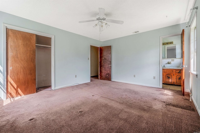 unfurnished bedroom featuring light carpet, ceiling fan, ensuite bath, and a closet