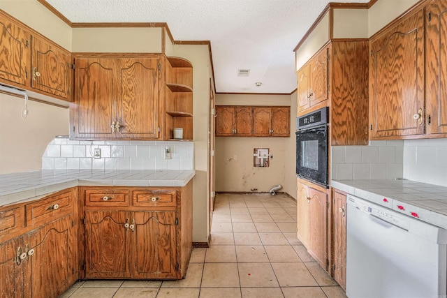 kitchen featuring white dishwasher, light tile patterned floors, backsplash, black oven, and tile counters