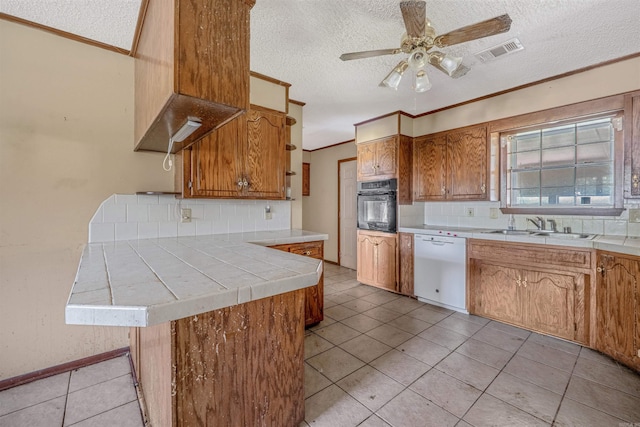 kitchen featuring a textured ceiling, kitchen peninsula, backsplash, white dishwasher, and black oven