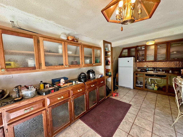 kitchen with a textured ceiling, sink, light tile patterned floors, and white fridge