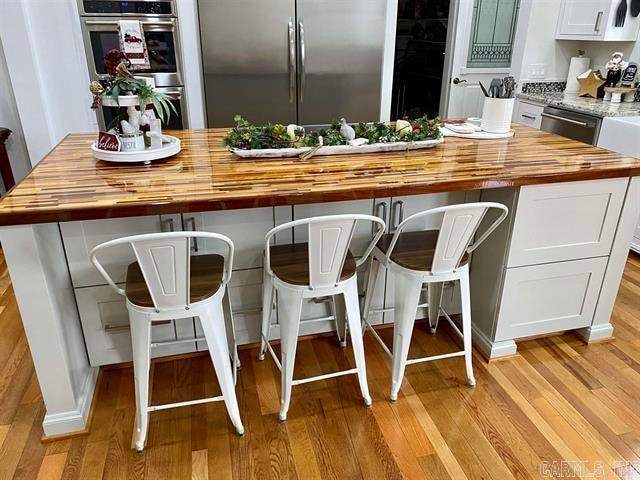 kitchen featuring white cabinetry, butcher block counters, a kitchen bar, light hardwood / wood-style flooring, and stainless steel appliances