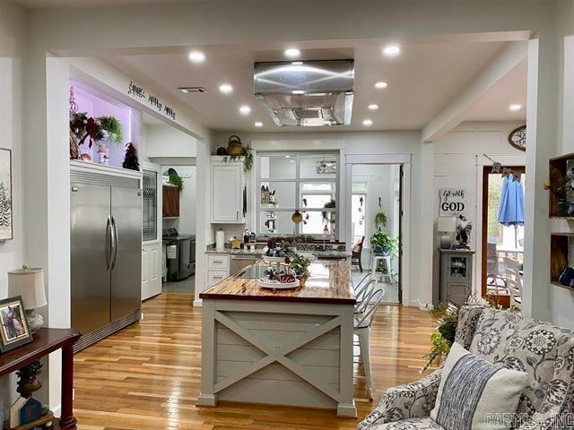 kitchen with light wood-type flooring, range, white cabinets, stainless steel built in fridge, and butcher block countertops