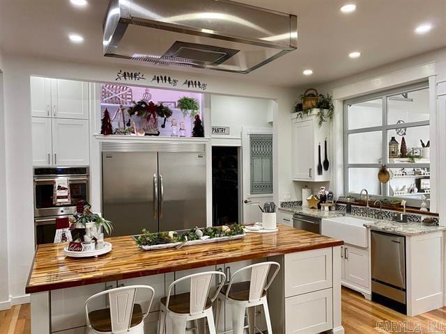 kitchen with white cabinetry, a center island, appliances with stainless steel finishes, and wooden counters