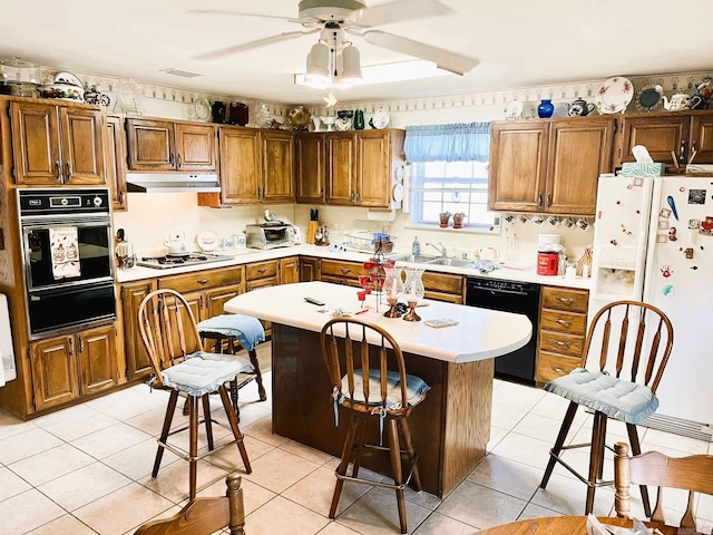 kitchen with a kitchen island, black appliances, ceiling fan, a breakfast bar, and light tile patterned floors