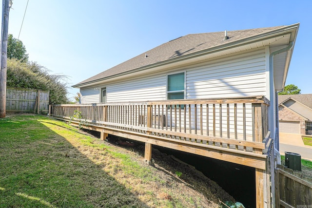 rear view of property with central AC unit, a garage, a wooden deck, and a lawn