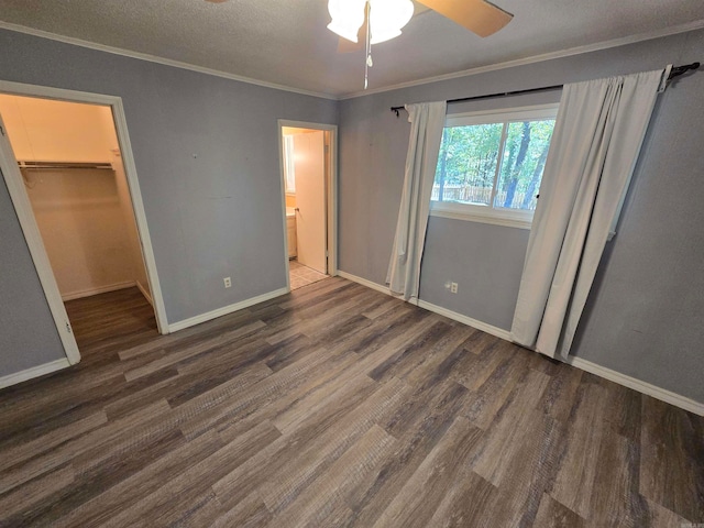 unfurnished bedroom featuring a closet, a walk in closet, dark hardwood / wood-style flooring, ornamental molding, and ceiling fan