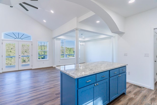 kitchen featuring blue cabinets, dark wood-type flooring, ceiling fan with notable chandelier, light stone countertops, and a center island