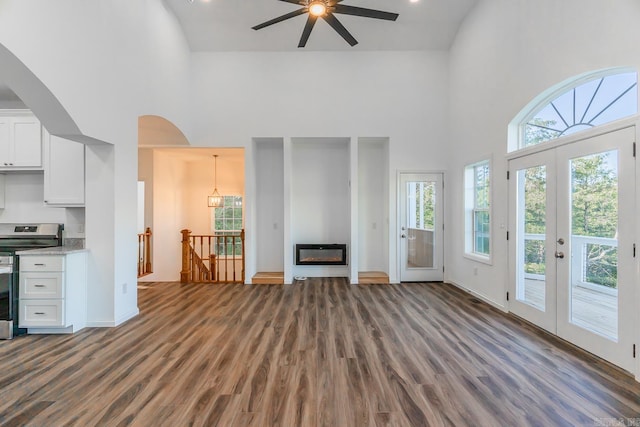 unfurnished living room featuring a towering ceiling, ceiling fan, dark hardwood / wood-style floors, and french doors