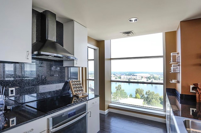 kitchen with oven, dark stone countertops, wall chimney exhaust hood, dark wood-type flooring, and white cabinetry