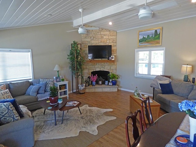 living room with lofted ceiling with beams, ceiling fan, wood-type flooring, wood ceiling, and a stone fireplace