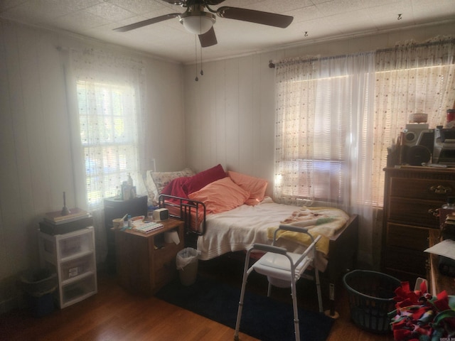 bedroom featuring ceiling fan, wood walls, ornamental molding, and wood-type flooring