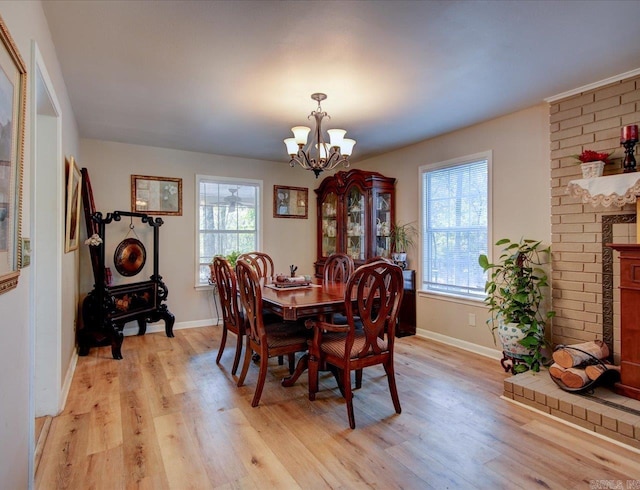 dining area with a brick fireplace, a notable chandelier, light hardwood / wood-style flooring, and a wealth of natural light