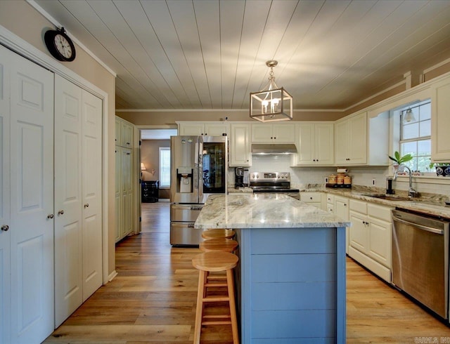 kitchen with a kitchen island, light stone counters, stainless steel appliances, sink, and pendant lighting