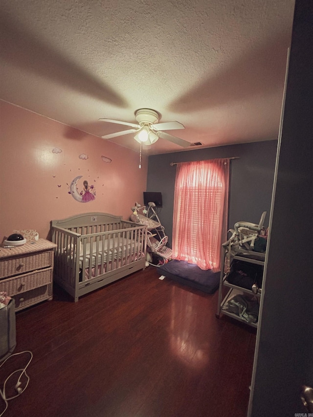 bedroom with a textured ceiling, a nursery area, wood-type flooring, and ceiling fan