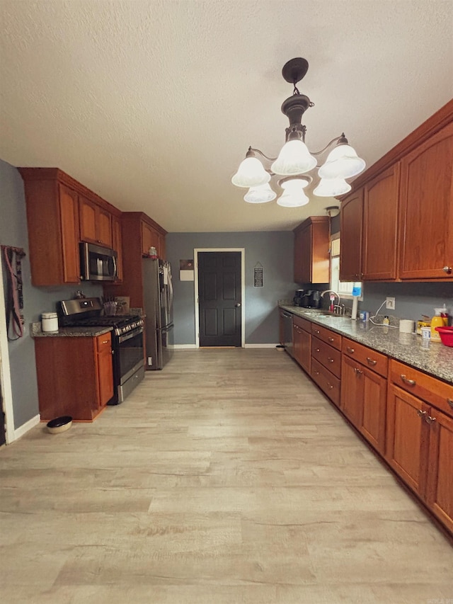 kitchen with appliances with stainless steel finishes, sink, an inviting chandelier, and light hardwood / wood-style flooring