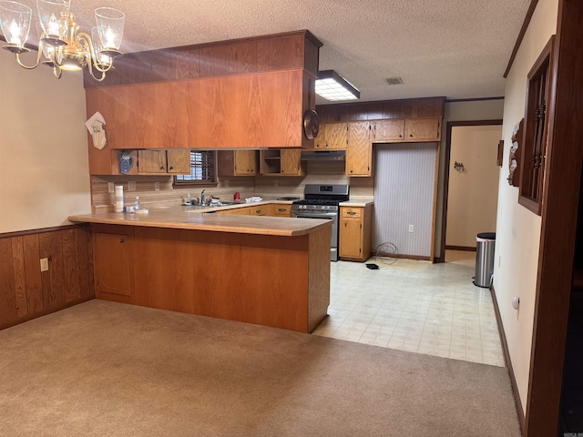 kitchen with gas stove, hanging light fixtures, kitchen peninsula, light colored carpet, and a textured ceiling