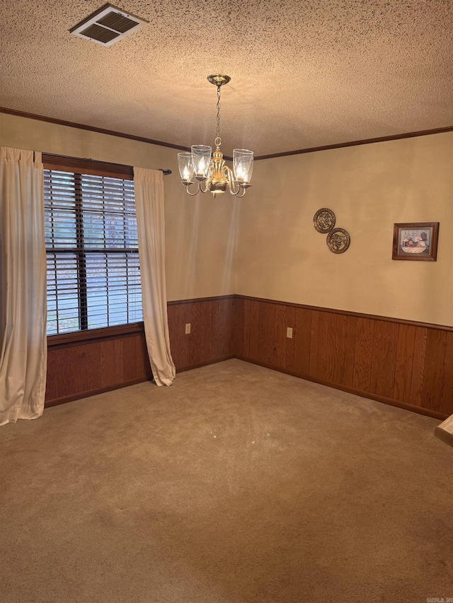 empty room with wood walls, crown molding, carpet flooring, a textured ceiling, and a notable chandelier