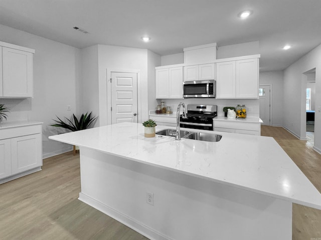 kitchen with white cabinetry, sink, stainless steel appliances, an island with sink, and light hardwood / wood-style floors