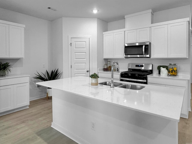 kitchen featuring a center island with sink, white cabinets, light wood-type flooring, appliances with stainless steel finishes, and light stone counters