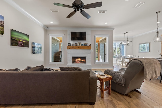 living room featuring ornamental molding, a fireplace, light hardwood / wood-style floors, and ceiling fan with notable chandelier