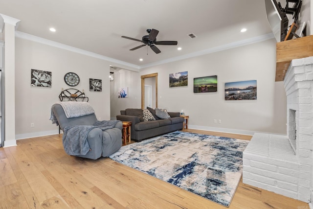 living room with a brick fireplace, crown molding, ceiling fan, and light hardwood / wood-style flooring