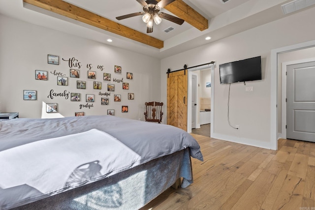 bedroom with a barn door, beamed ceiling, ceiling fan, hardwood / wood-style floors, and ensuite bath