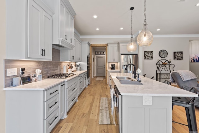 kitchen featuring pendant lighting, an island with sink, sink, appliances with stainless steel finishes, and light wood-type flooring