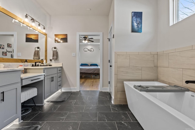 bathroom with ceiling fan, vanity, a tub to relax in, and tile walls