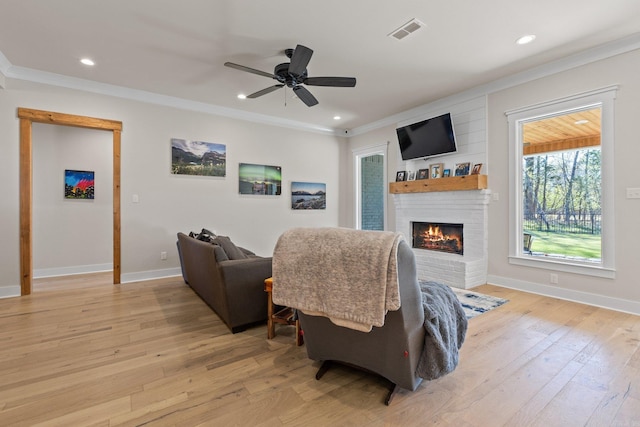 living room featuring a fireplace, crown molding, light wood-type flooring, and ceiling fan