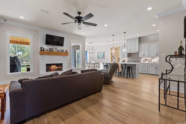 living room featuring a fireplace, ceiling fan with notable chandelier, ornamental molding, and light hardwood / wood-style flooring